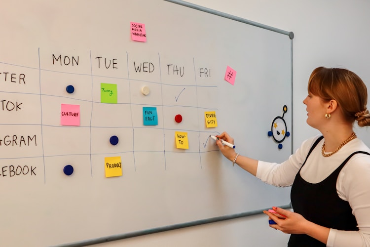 a woman writing on a white board with sticky notes