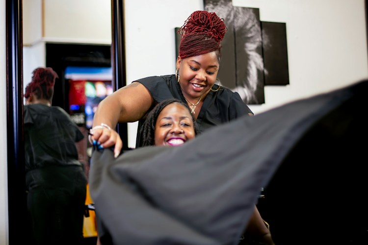 Stylist drapes client with a black cape in salon
