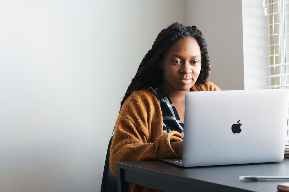 A woman with long braids using a laptop at a desk in a workspace