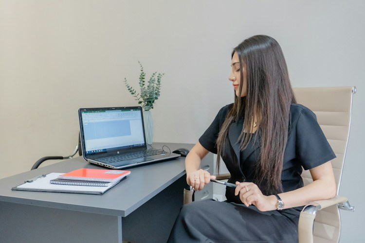 Woman in black dress working at desk with laptop
